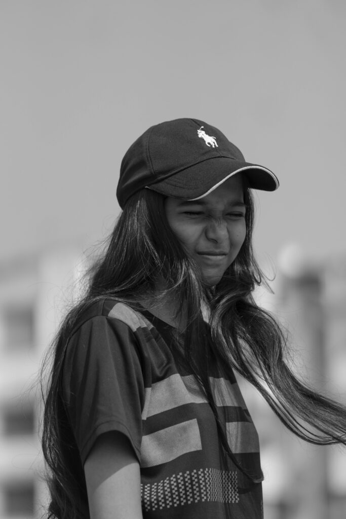 Black and white portrait of a teen girl wearing a cap with long hair, expressing urban style.